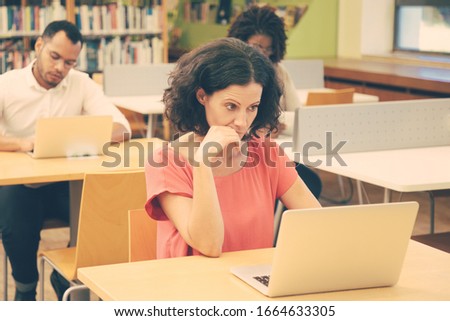 Adult students working on computer during class. Multiethnic man and women sitting at desk and using laptops. Bookshelves in background. Education concept