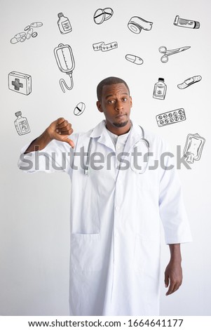 Black doctor showing thumb down with hand drawn medical sketches. Harm to health concept. Isolated front view with medicine icons on background.