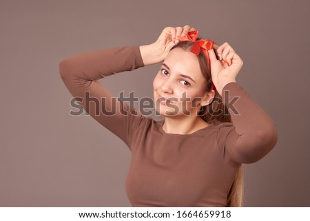 christmas shoot of funny blonde girl with pois bow on her head, adorned like a xmas gift, wearing elegant red dress and bracelet