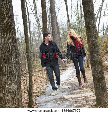A couple walking hand in hand through a woodland in winter.