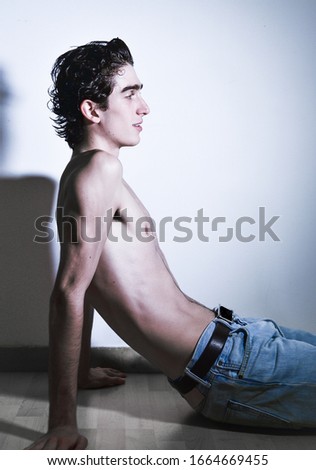 expressive mediterranean Italian dark haired handsome male model boy with angel face and fit sportive body posing for casual fashion shooting on wooden floor wearing blue jeans