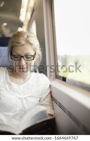 A woman sitting by a train window, reading a book.