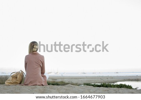 Blond woman sitting on a sandy beach.