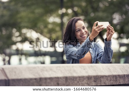 A woman taking a photograph or a selfie with a smart phone