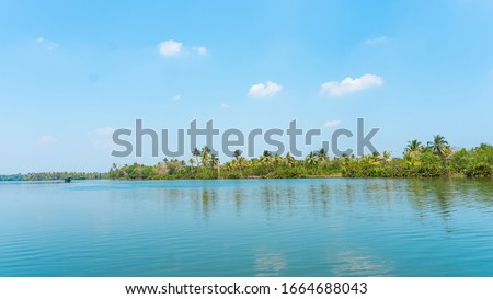 A picture of a beautiful tropical green forest island with bright blue sky, slight of clouds and clear water. A lot of coconut trees are present gives a refreshing and relaxed mood to the environment.
