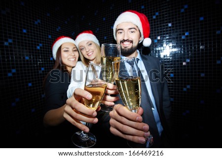 Three business partners in Santa caps toasting with champagne in nightclub 