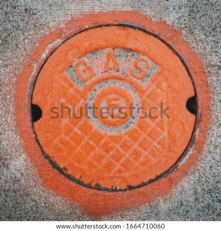 A gas manhole cover, round and painted orange on the road in Seattle.