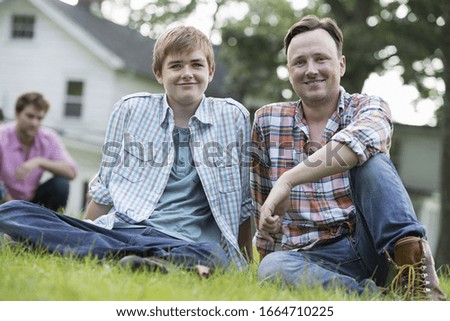 A father and son at a summer party, sitting on the grass.