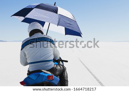 A motorcyclist sheltering under an umbrella, on the start line at Speed Week, on the Bonneville Salt Flats.