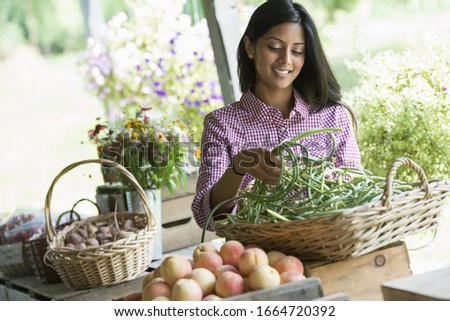 A farm stand with fresh organic vegetables and fruit. A woman holding bunches of carrots.