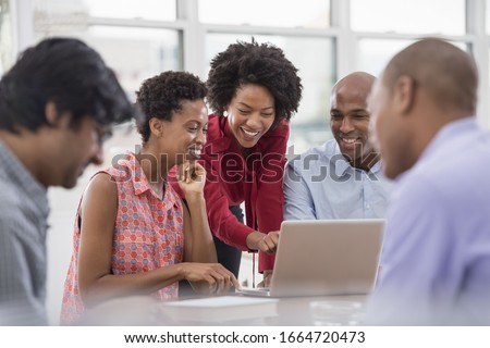 A business environment, a light and airy workplace in the city.A group of people, men and women at a meeting, using a laptop.