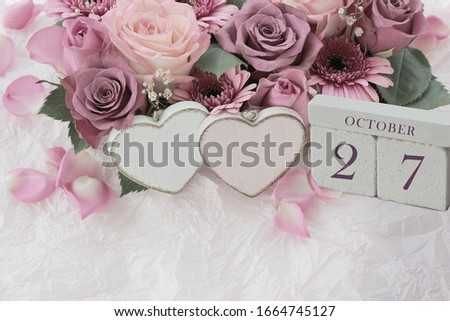 Calendar. October 27th. Wood cube calendar with date of month and day, pink flowers bouquet and two hearts. Greeting card for various holidays. Invitation. Copy space.
