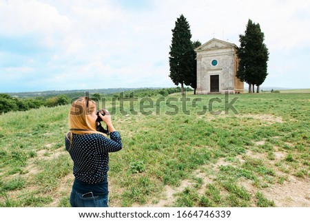 Young female traveler taking a photo of a famous church in fields of Tuscany, Italy