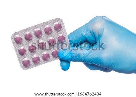 Surgeon's hand in a blue medical glove holds a blister of tablets isolated on a white