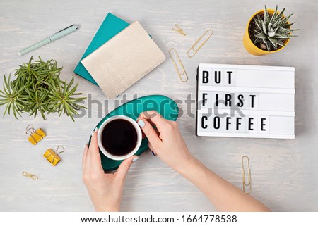 Flat lay with lightbox with text "But first coffee" and coffee cup in woman hand. Social media, feminine blog, morning of workday concept. Top view