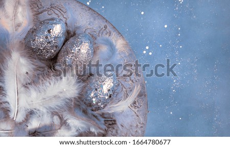 unfocused easter eggs, feathers with festive glitter confetti on creative toned in blue color background, happy easter concept