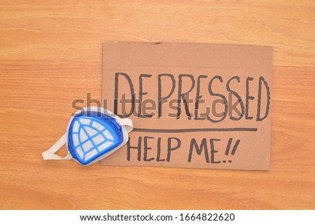 Handwritten cardboard sign (Depressed Help Me) next to face mask on wood grain background