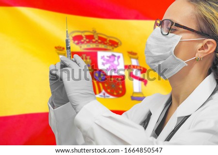 Female doctor or nurse in gloves holding syringe for vaccination against the background of the Spain flag. Medicine concept and fight the virus. Coronavirus in Spain.