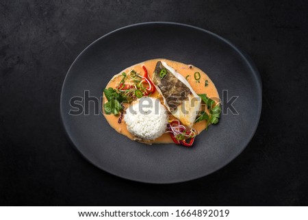 Gourmet fried skrei cod fish Thai curry with jasmine rice and chili as top view on a modern design plate with copy space 