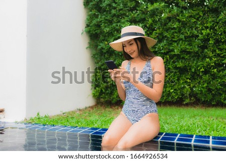Portrait young asian woman using smart mobile phone around outdoor swimming pool in hotel resort
