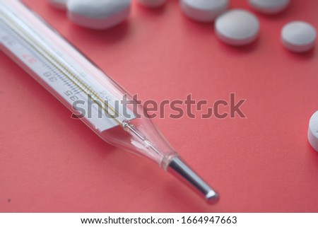 Close up of thermometer and pill on red background 