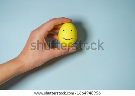 hand holding smiley egg on blue background; easter celebration concept.