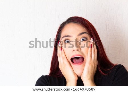 White and redhead Hispanic woman surprised and scared holding her face with her hands
