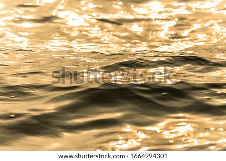 Water surface with moving wave of golden water reflecting 
with sunlight background