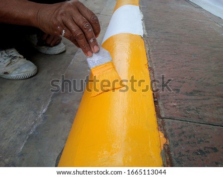Hands are painted pavement edge - close-up. Workers hand holding a paint brush into yellow on the edge of the sidewalk. On concrete background with copy space Focus.

