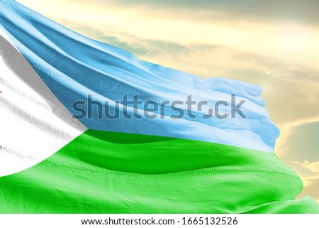 Djibouti national flag cloth fabric waving on the sky with beautiful sun light - Image