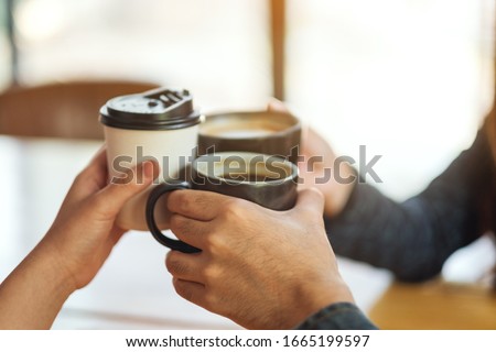 Closeup image of people enjoyed drinking and clinking coffee cups on the table in cafe