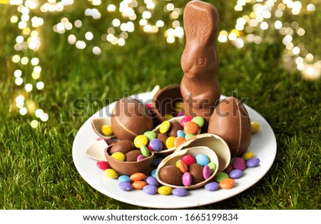 easter, sweets and confectionery concept - plate with chocolate bunny, eggs and candy drops on grass