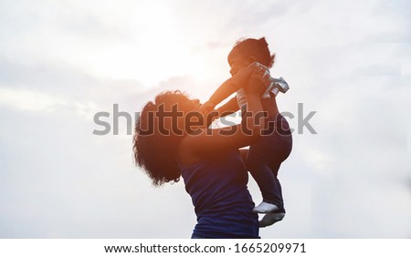 Happy african mother playing with her daughter outdoor - Afro mum and child having fun together - Family, happiness and love concept - Focus on faces Royalty-Free Stock Photo #1665209971