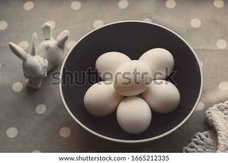 White chicken eggs in a round navy blue bowl with a white edging, shot from above on a background of gray fabric with white polka dots, use: Easter decor, kitchen