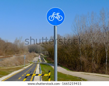 selective focus on blue traffic sign. circular metal bicycle route road and traffic sign with white bicycle symbol on aluminum post. paved asphalt path in diminishing perspective. spring nature scene