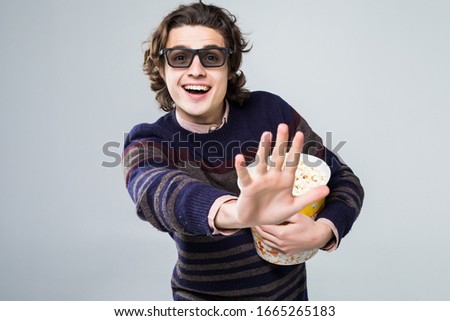 Young handsome man with beard over isolated white background with 3d glasses and holding a big bucket of popcorns while pointing front