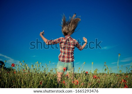 Beautiful girl in poppy field. Young girl with long hair among the blossoming poppy field. Girl jumping