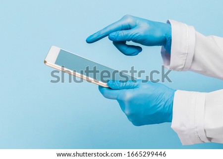 Female hand in a  medical glove holds a blank modern tablet on a blue background. Mock up.