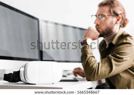 Selective focus of vr headset on table near 3d artist looking at computer monitor on table isolated on grey