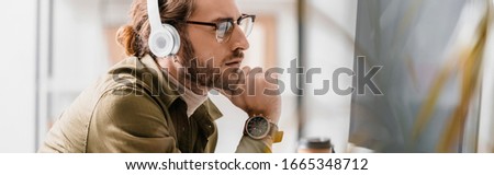 Side view of pensive 3d artist in headphones looking at computer monitor, panoramic shot