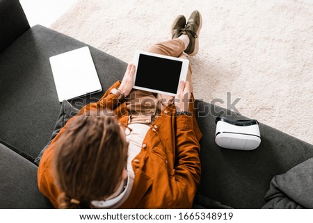 Overhead view of 3d artist holding digital tablet with blank screen near laptop and vr headset on couch