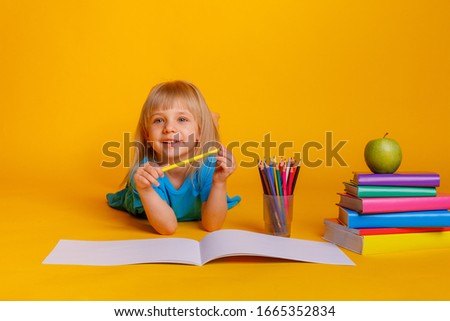 child girl draws colored pencils on a yellow background. Concept of preschool education