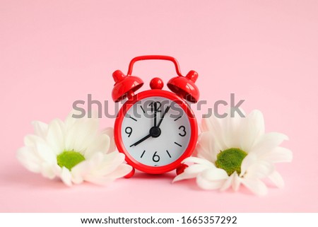 Concept of early spring, red alarm clock with flowers on a pink background