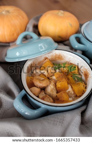 Roast pumpkin and chicken with spices in a blue pan on a wooden table, top view. Thanksgiving concept
