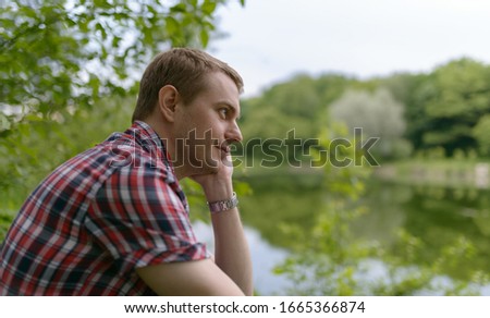 Young pensive man looks at the river. Unity with nature.