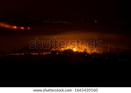 Mountains in fog at beautiful night in autumn in Dalat city, Vietnam. Landscape with Langbiang mountain valley, low clouds, forest, colorful sky with stars, city illumination at dusk.