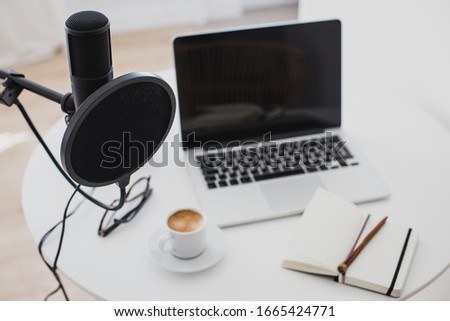 Items for recording podcast: professional microphone, earphones and laptop on white table in cozy home studio.
