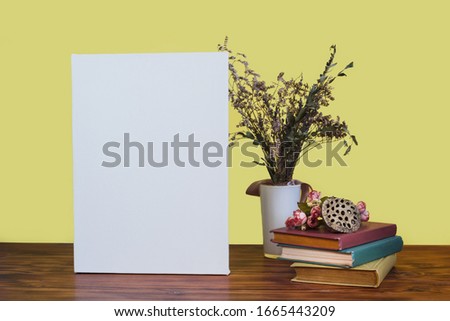 Blank vertical canvas, books and flowers on table. Mockup poster against bright yellow wall.