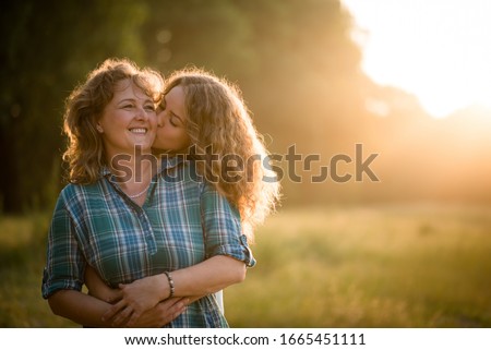 Pretty daughter embracing her mother from behind and kissing