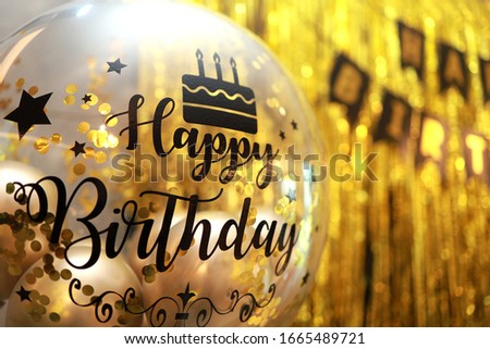 Selective focus image of transparent balloon with Happy Birthday text on Golden backdrop design.